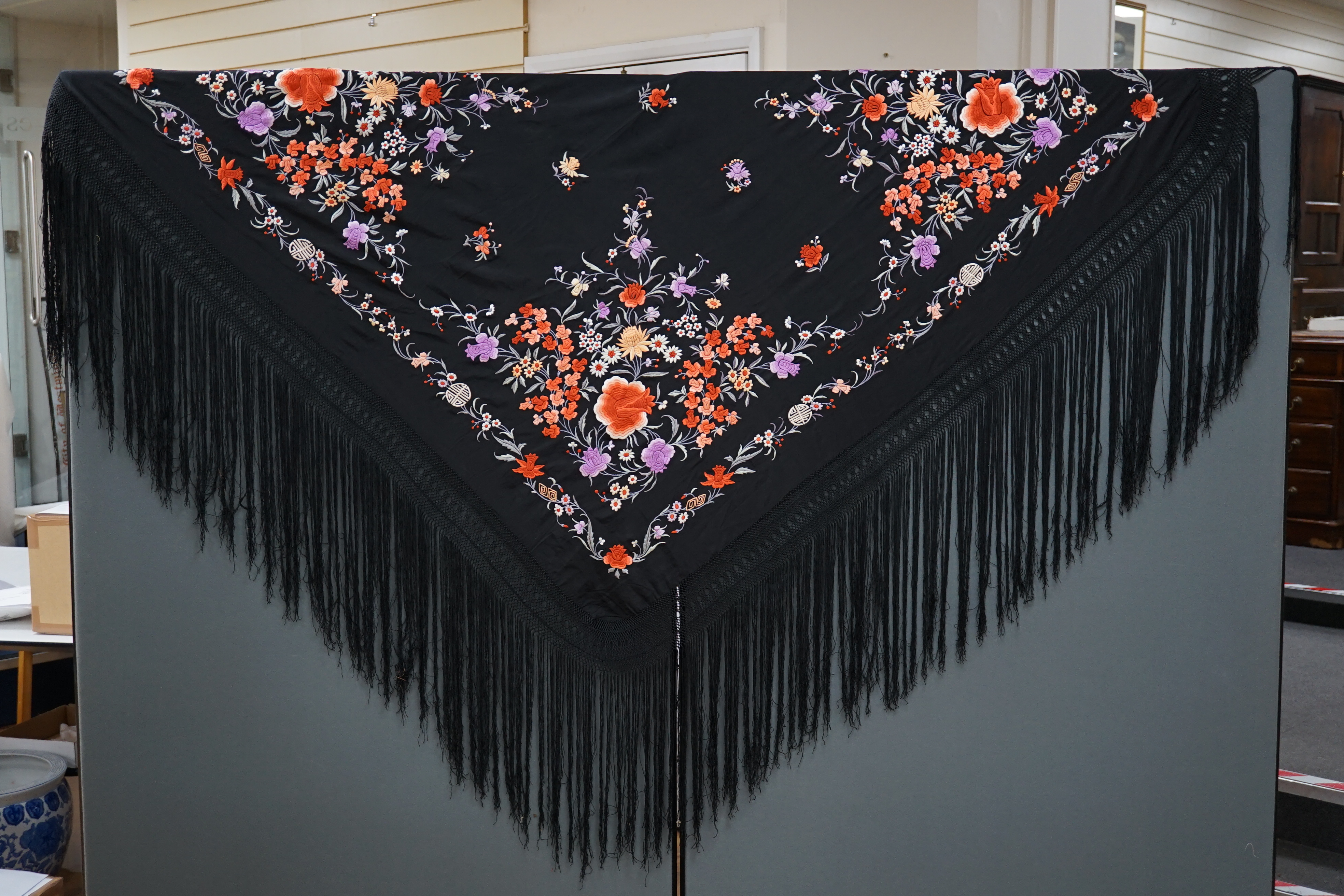 A late 19th / early 20th century Chinese black silk shawl, with polychrome silk embroidered flowers in green, red, orange, lilac, yellow and white, the centre embroidered with, sprigs of multi-coloured flowers, the four